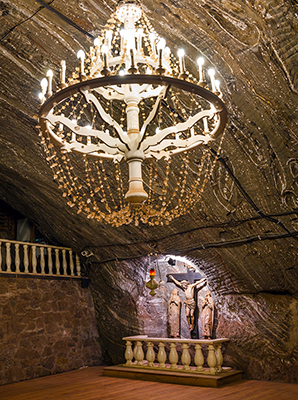 Zdjęcie przedstawia zdobiony żyrandol i ołarz w podziemnej komnacie kopalni.