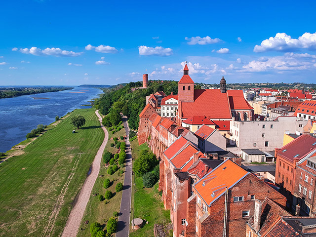 Zdjęcie przedstawia rzekę, bulwary i zabudowania miejskie.