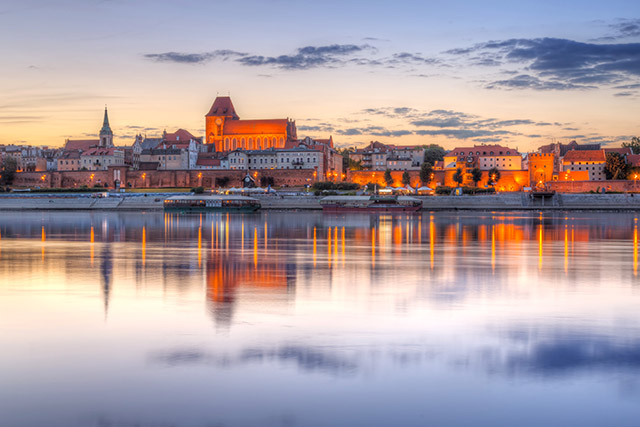 Zdjęcie przedstawia panoramę miasta odbijającego się w wodzie o zmierzchu.